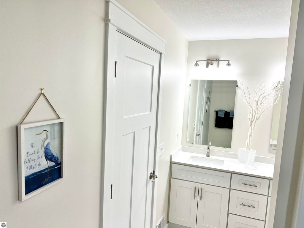 Interior view of a modern bathroom featuring a white vanity with a sink, a large mirror, and decorative elements including a framed artwork of a blue heron on the wall, emphasizing comfort and style in the home at 2757 Fashion Avenue, Interlochen, MI.