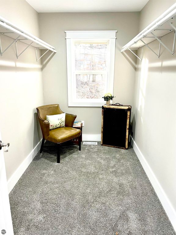 Cozy corner of a home featuring a brown armchair, a small table with a flower vase, and two wall-mounted shelves, illuminated by natural light from a window, ideal for a reading nook or study space.