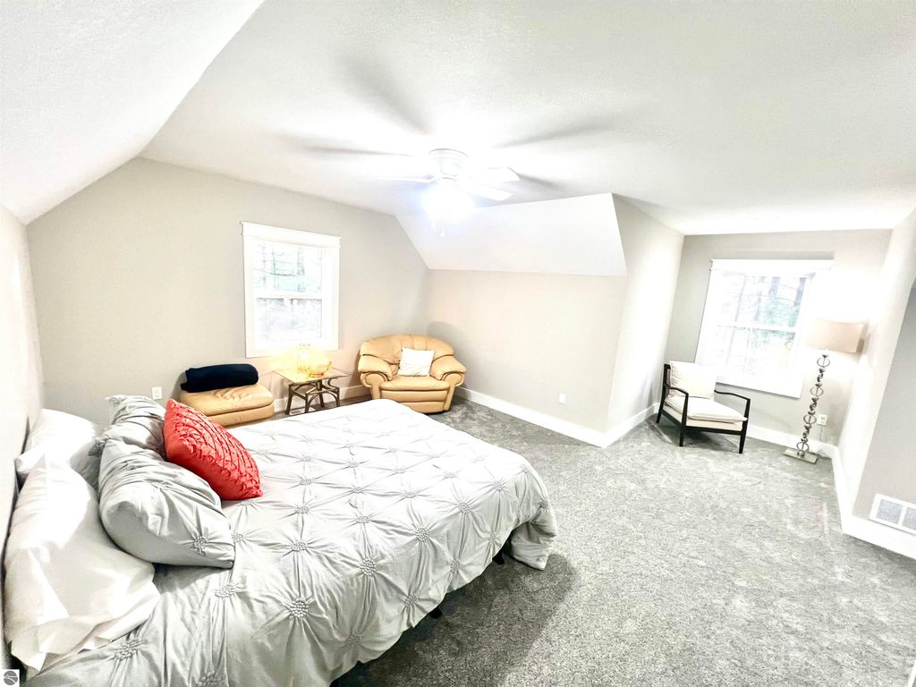 Spacious bedroom in a well-constructed home featuring a queen-sized bed, cozy seating area, and natural light from multiple windows, ideal for family comfort and relaxation.