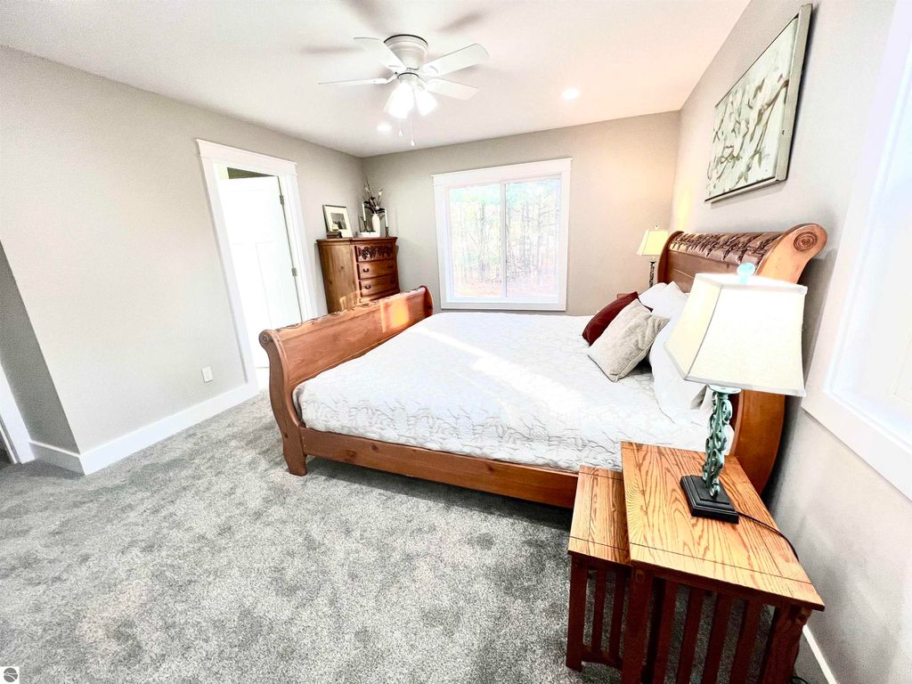 Spacious bedroom in a modern home featuring a wooden sleigh bed, bedside table with lamp, and large window overlooking a wooded area, emphasizing comfort and family-friendly design.