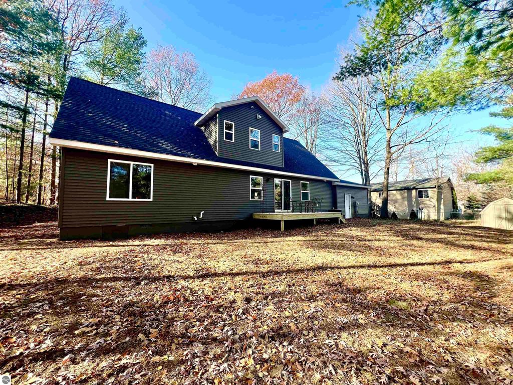 Spacious home exterior at 2757 Fashion Avenue, Interlochen, MI, featuring a well-maintained yard, large windows, and a deck, surrounded by trees in a tranquil neighborhood.