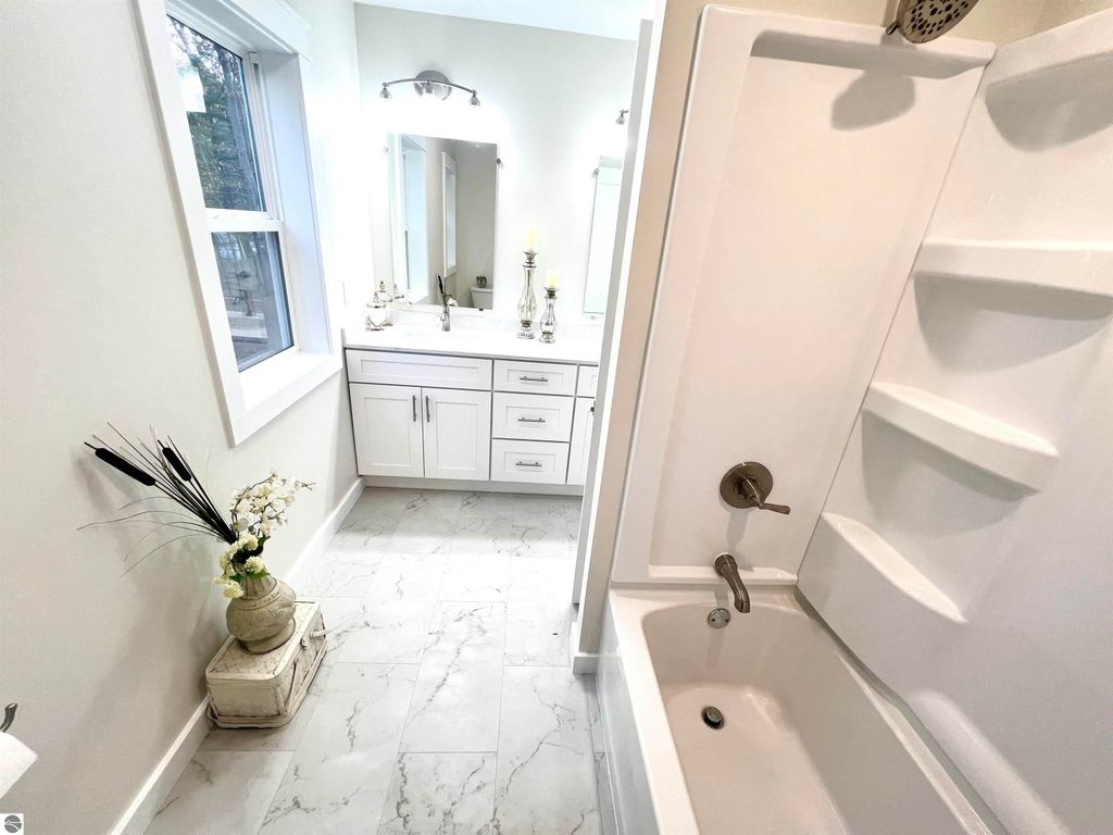 Modern bathroom interior featuring a white bathtub, sleek vanity with mirror, and decorative plants, showcasing the spacious design and contemporary amenities of the property at 2757 Fashion Avenue, Interlochen, MI.