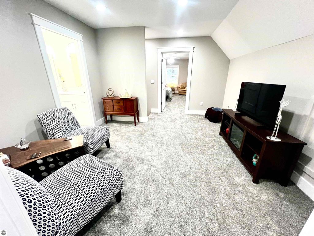 Spacious family room with two patterned chairs, a wooden side table, and a TV stand, featuring plush carpet and light gray walls, showcasing comfort in the home at 2757 Fashion Avenue, Interlochen, MI.