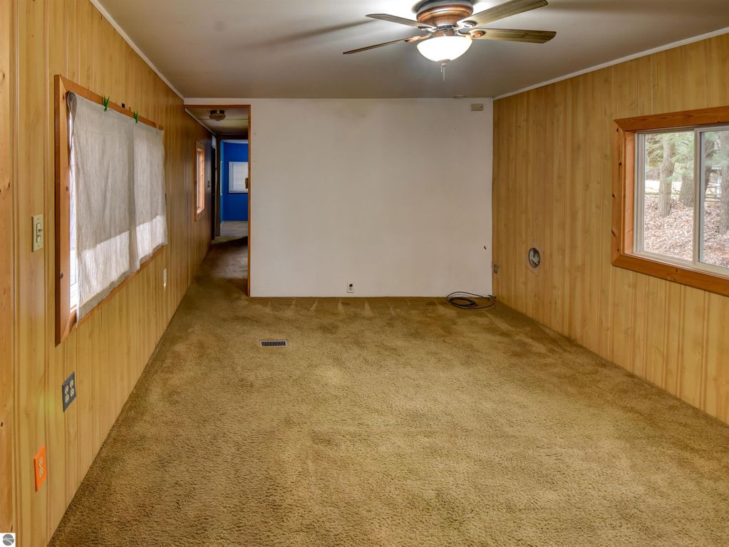Interior view of a cozy living space in a Tawas City home, featuring wooden paneling, beige carpet, and a ceiling fan, with windows allowing natural light and a glimpse of the outdoors.