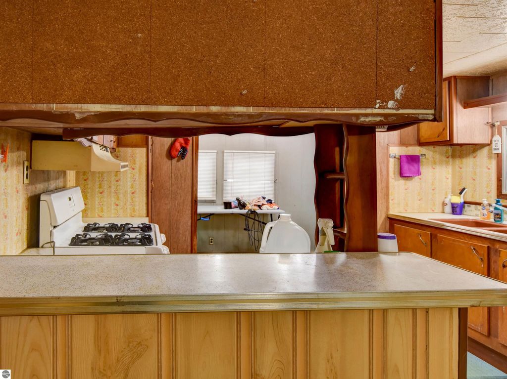 Kitchen view showcasing gas stove, wooden cabinetry, and adjoining room with natural light, relevant to listing of 2 bedroom home at 974 Parkway Drive, Tawas City, MI.
