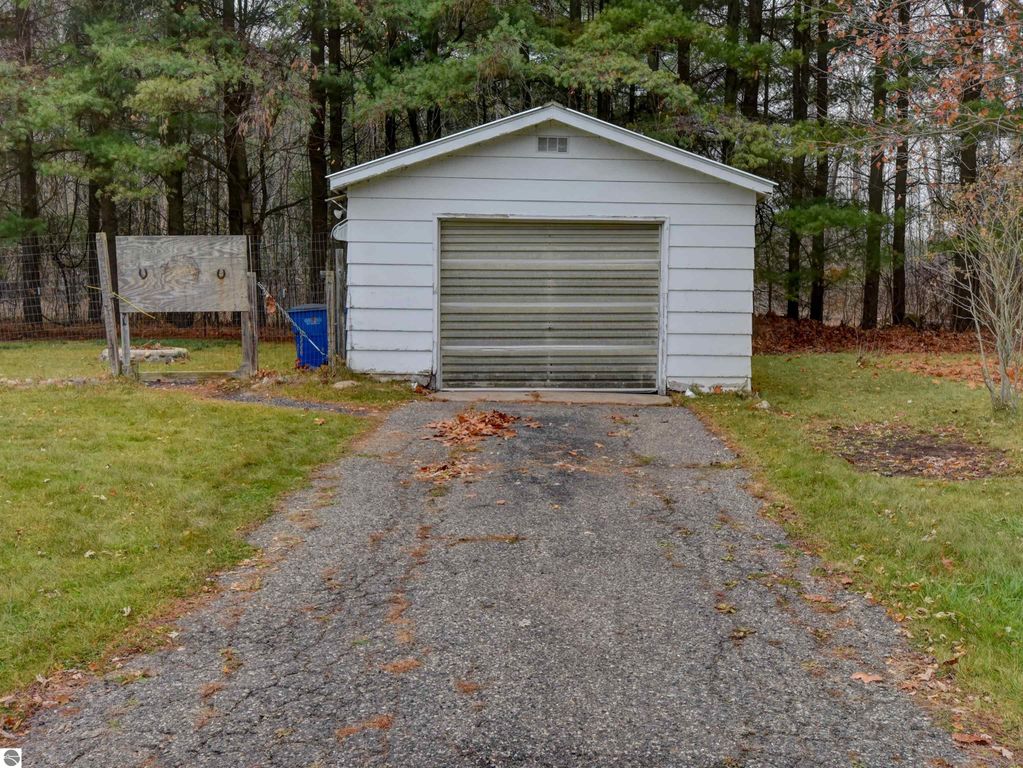 Garage with a cement floor and a driveway, surrounded by a fenced yard and trees, located at 974 Parkway Drive, Tawas City, MI, ideal for hobbies and pets.