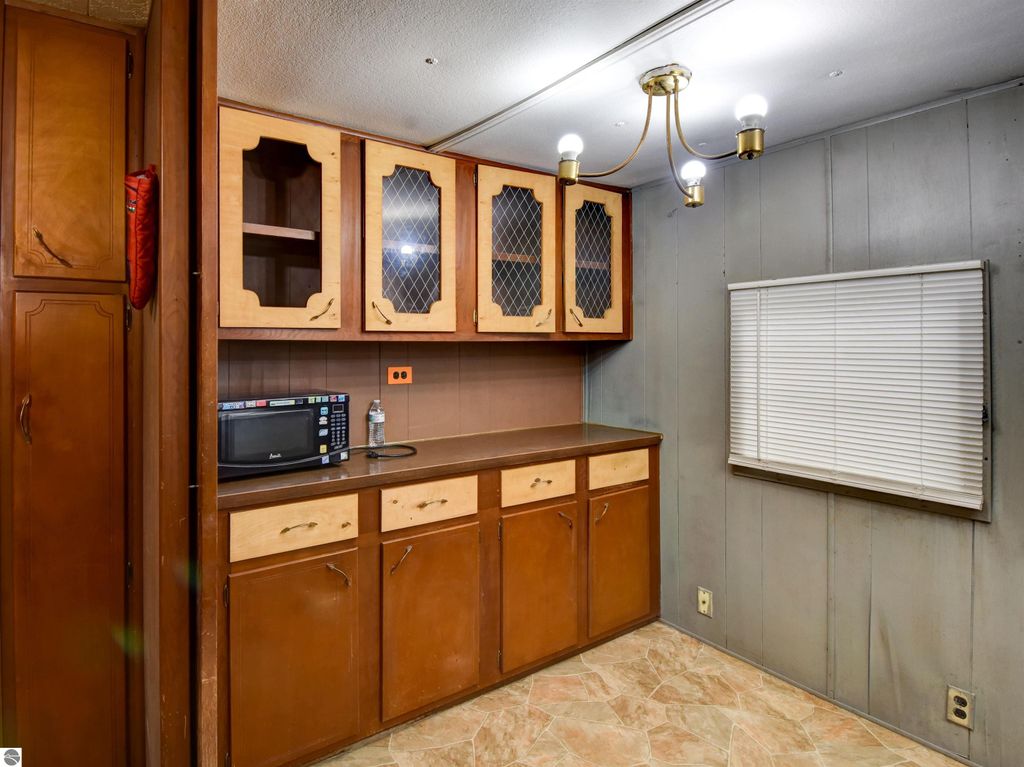 Interior view of a kitchen area featuring wooden cabinets, a countertop with a microwave, and a window with blinds, suitable for a starter home at 974 Parkway Drive, Tawas City, MI.