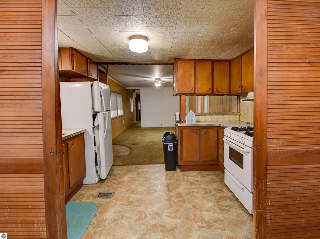 Kitchen interior of a 2-bedroom home at 974 Parkway Drive, featuring white appliances, wooden cabinetry, and a spacious layout, ideal for a starter house in Tawas City, MI.