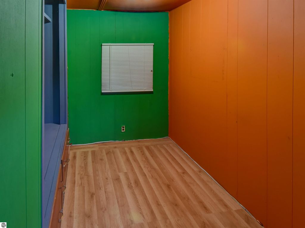Colorful interior of a room featuring green and orange walls, hardwood flooring, and a window with blinds, suitable for a starter home at 974 Parkway Drive, Tawas City, MI.