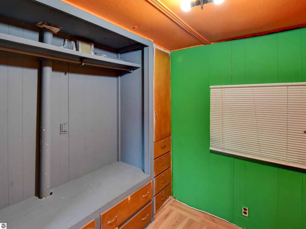 Interior view of a bedroom with green walls, orange ceiling, built-in shelving, and wooden drawers, showcasing potential for updates in the Tawas City property listing.