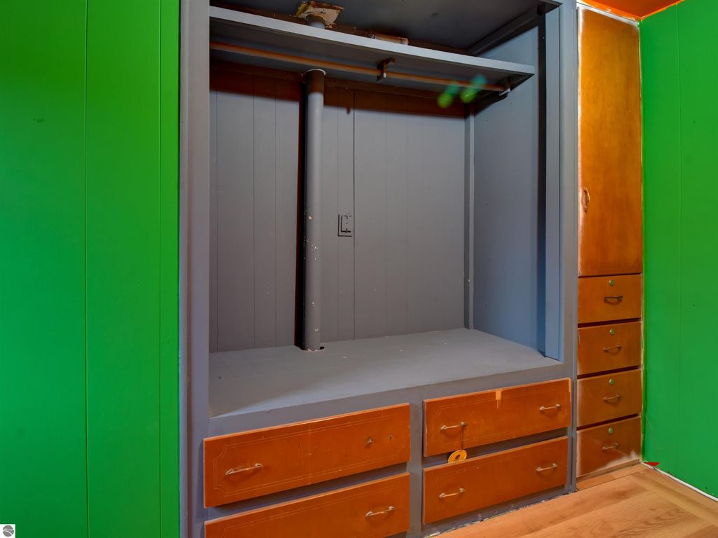 Interior view of a bedroom closet featuring a gray hanging rod, orange drawers, and green walls, illustrating storage space in the 2-bedroom home at 974 Parkway Drive, Tawas City, MI.