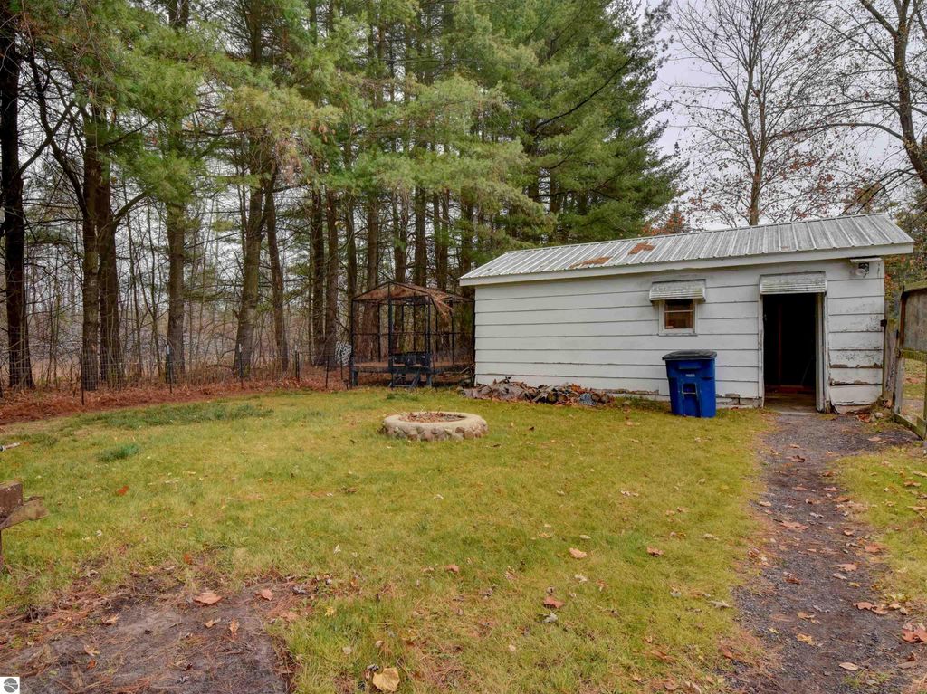 Fenced yard with a shed and fire pit, surrounded by trees, near 974 Parkway Drive, Tawas City, MI, ideal for pets and outdoor activities.