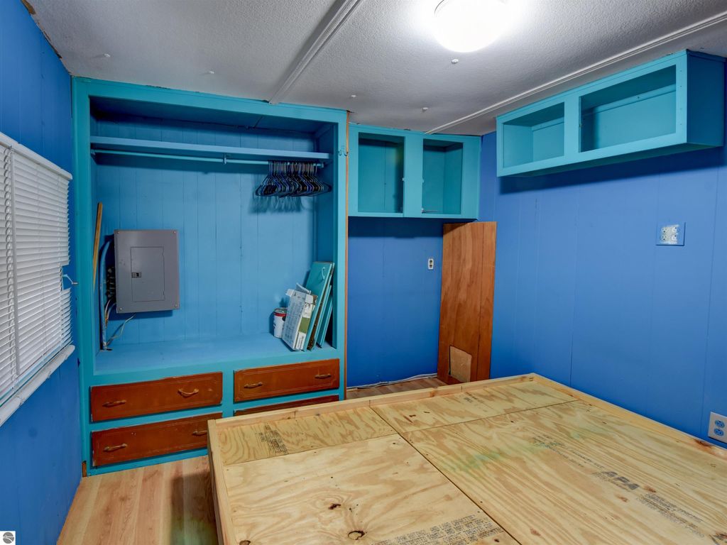 Interior view of a blue room featuring a built-in closet with wooden drawers, shelving, and a plywood floor, suitable for a starter home at 974 Parkway Drive, Tawas City, MI.