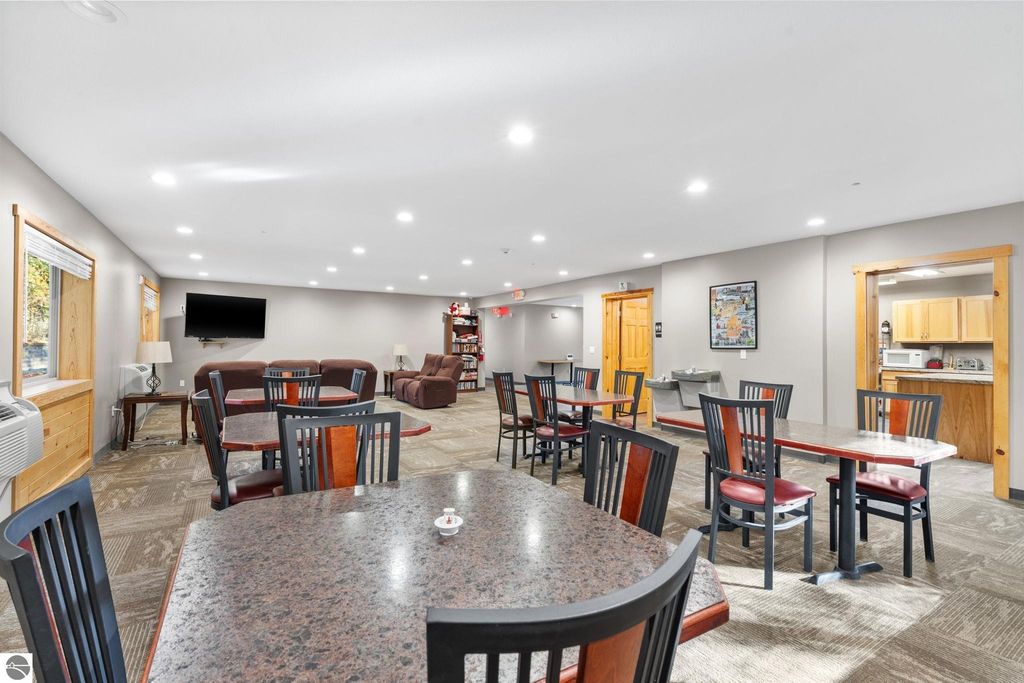 Dining area with tables and chairs, featuring a television and access to a kitchenette, showcasing the updated common space of a motel property near Torch Lake, ideal for guest gatherings and relaxation.