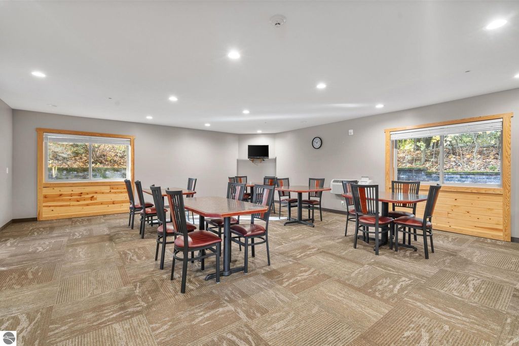 Dining area in updated motel featuring tables and chairs, large windows, and a wall-mounted clock, highlighting potential guest accommodations near Torch Lake.