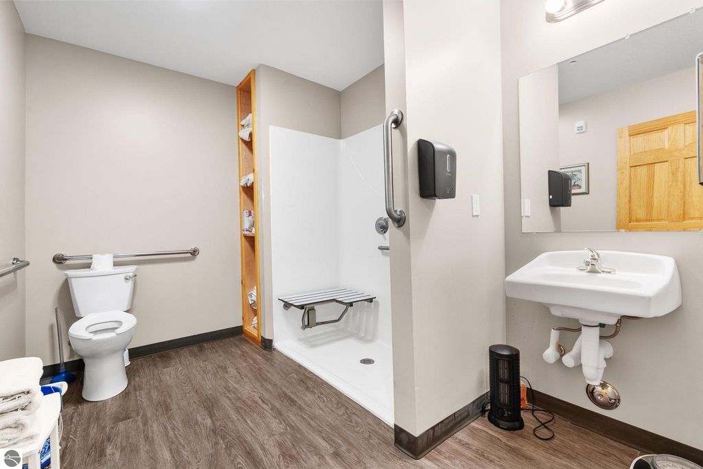 Accessible bathroom featuring a toilet, sink, and roll-in shower with grab bars, designed for comfort and convenience in a motel setting near Torch Lake.