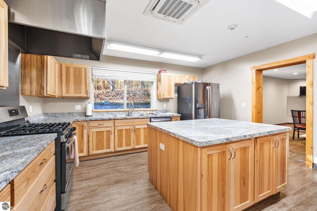 Modern kitchen with wooden cabinetry, granite countertops, stainless steel appliances, and a large island, showcasing a bright and inviting space ideal for a resort property investment near Torch Lake.