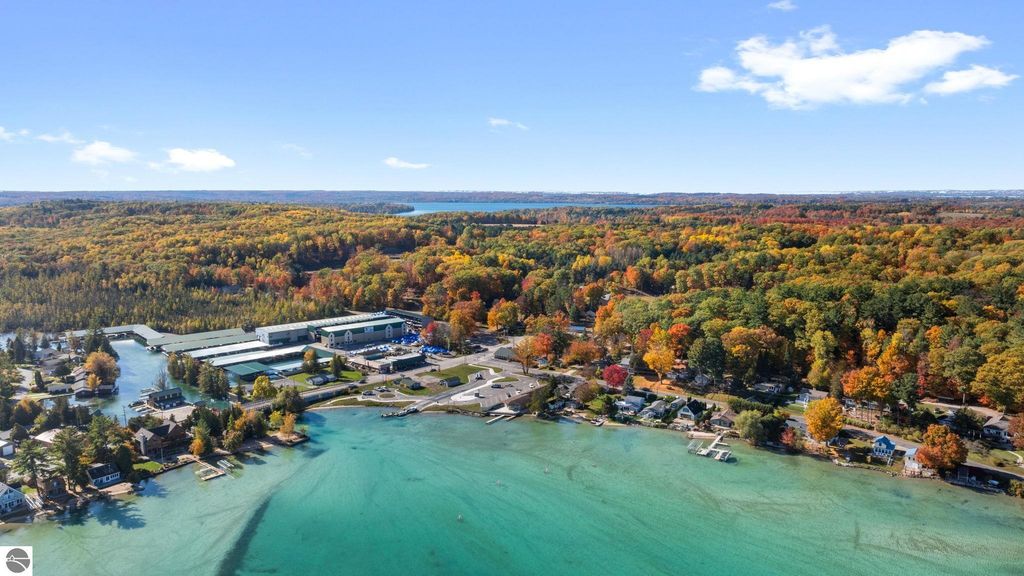 Aerial view of Torch Lake area in Rapid City, Michigan, showcasing vibrant fall foliage, nearby residential properties, and commercial buildings along the waterfront, emphasizing the scenic location and investment potential of the resort property listed at 12800 & 12862 Cherry Avenue.