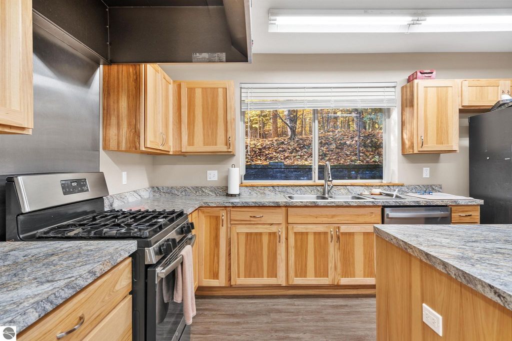 Modern kitchen with wooden cabinets, stainless steel appliances, granite countertops, and large window showcasing wooded view, highlighting property features for potential investment at 12800 & 12862 Cherry Avenue, Rapid City, MI.