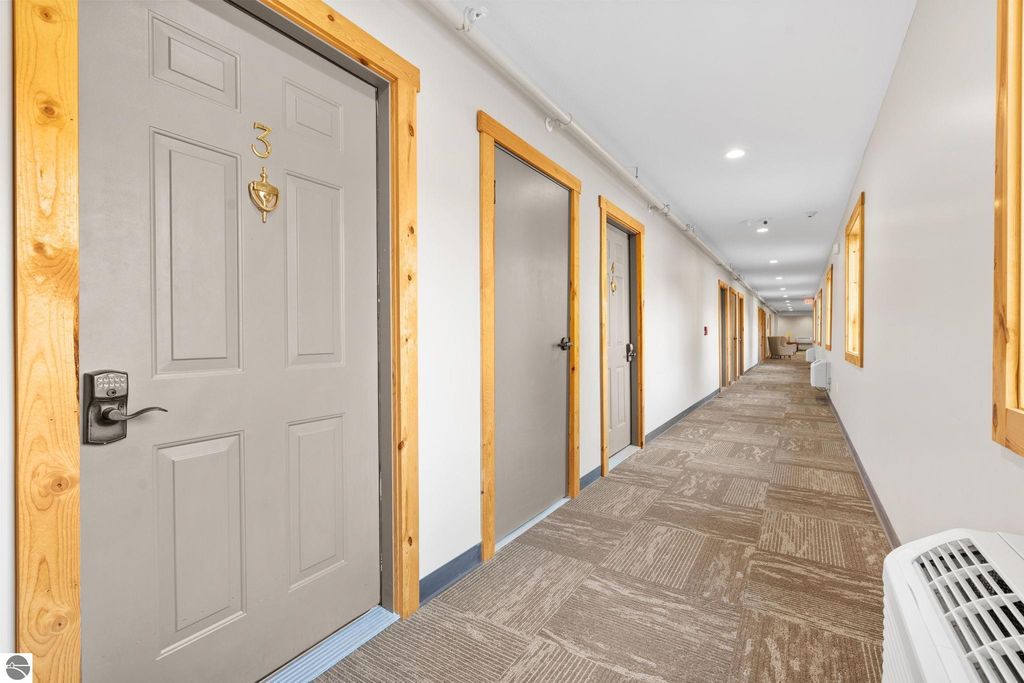 Hallway of a motel featuring multiple guest room doors, including door number 3, with modern decor and ample lighting, showcasing a well-maintained lodging environment near Torch Lake, suitable for investment opportunities.
