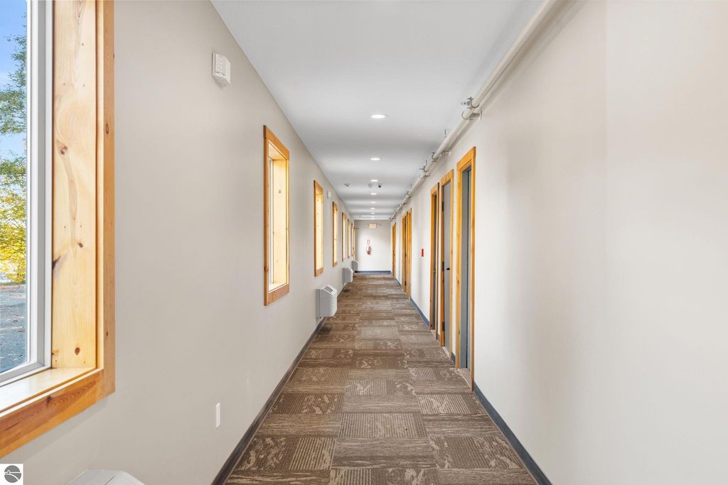 Interior hallway of a motel with wooden trim, windows allowing natural light, and multiple guest room doors, showcasing the updated accommodations available at 12800 & 12862 Cherry Avenue, Rapid City, MI.