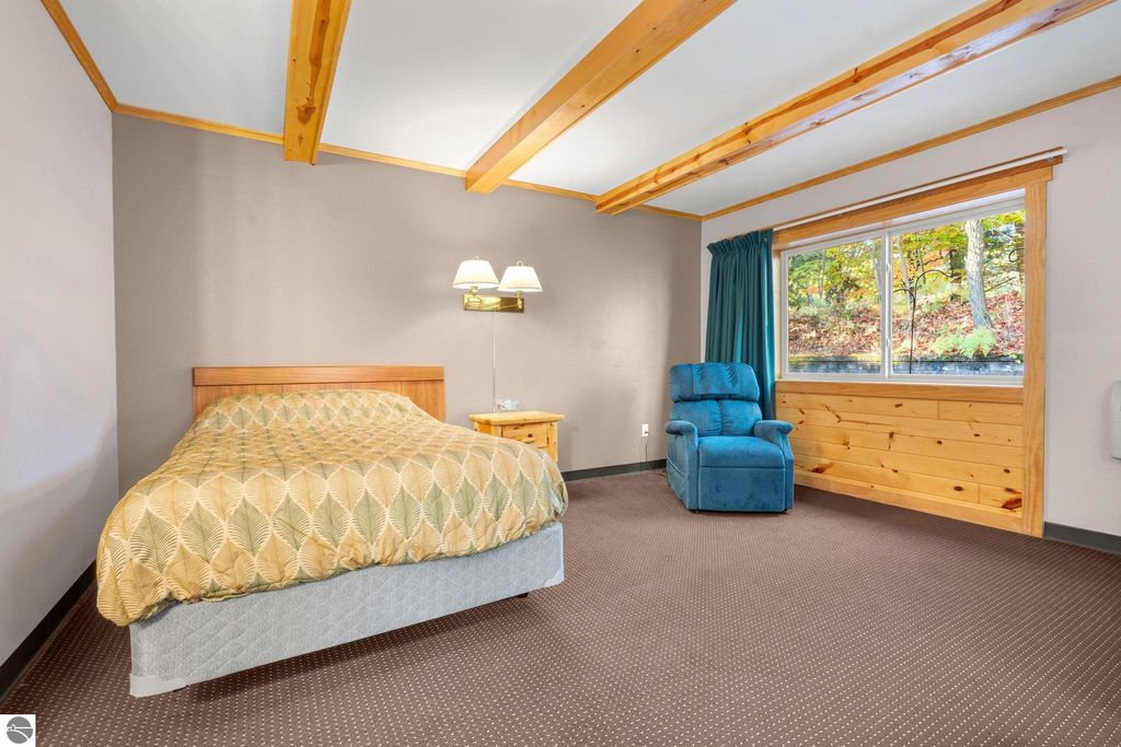 Cozy motel room featuring a queen-sized bed, blue recliner, and large window with scenic views, highlighting the updated accommodations for guests near Torch Lake.