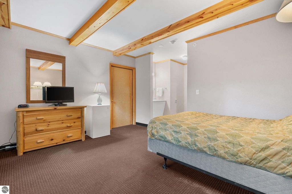 Updated motel room featuring wooden furnishings, a television, and a queen-sized bed, showcasing a cozy atmosphere ideal for guests near Torch Lake.