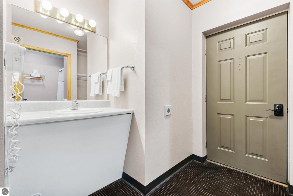 Bathroom area with sink, mirror, and entrance door, featuring towels and hairdryer, suitable for motel accommodations near Torch Lake.