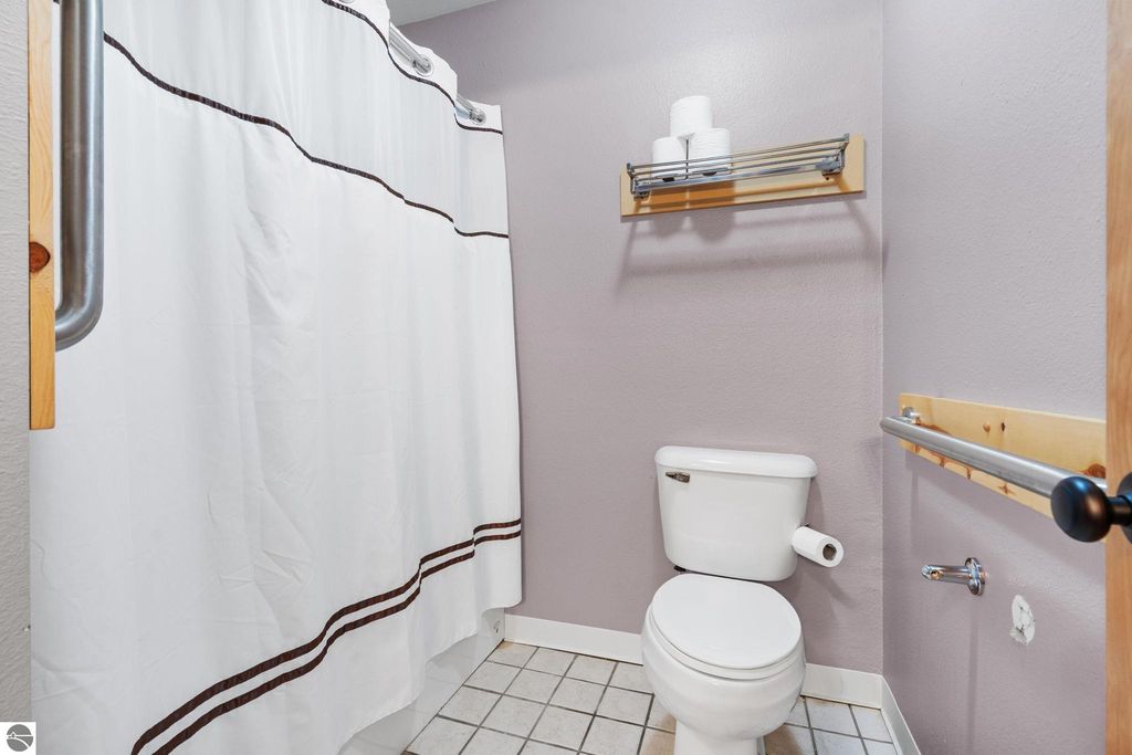 Bathroom interior featuring a toilet, shower curtain, towel rack, and neutral-colored walls, highlighting amenities for the motel at 12800 & 12862 Cherry Avenue, Rapid City, MI.
