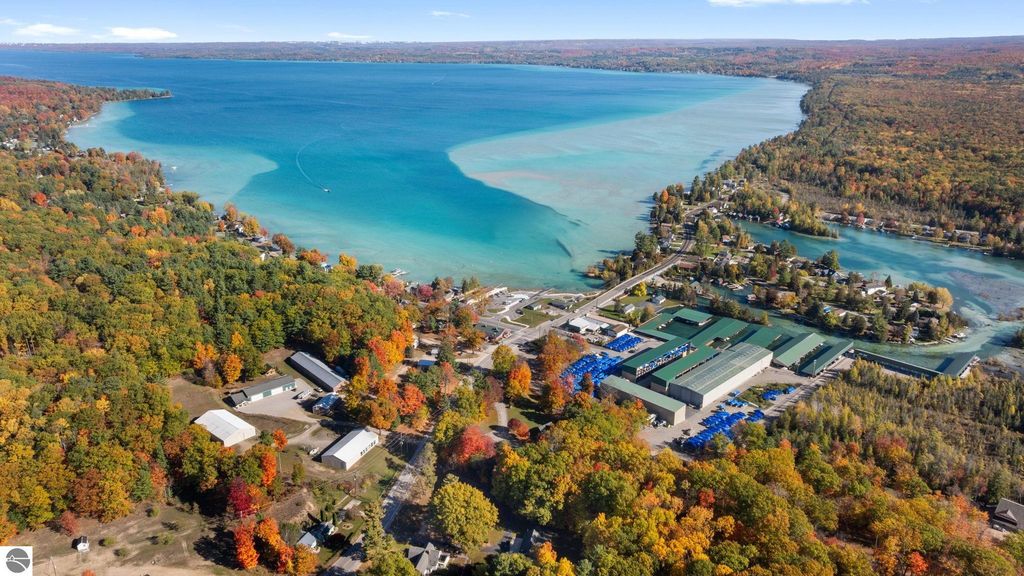 Aerial view of Torch Lake showcasing vibrant autumn foliage, clear blue waters, and nearby resort properties, including a motel and residential areas, highlighting the investment potential in Rapid City, MI.