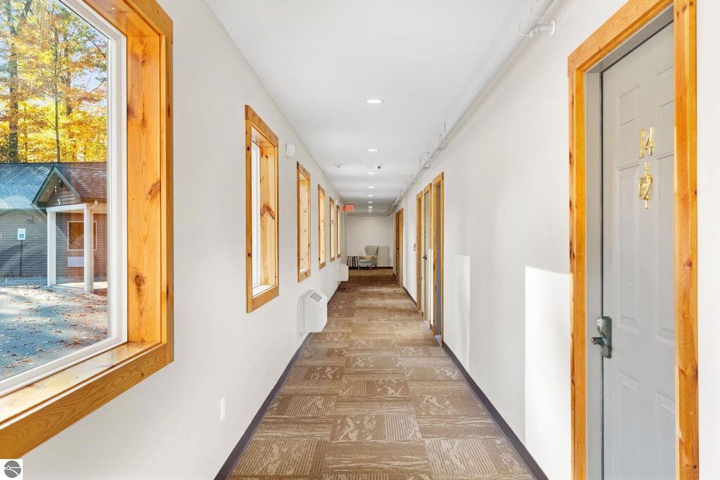 Interior hallway of a motel featuring wooden-framed windows, doors labeled with room numbers, and a seating area, showcasing the updated design and layout of the property at 12800 & 12862 Cherry Avenue, Rapid City, MI.