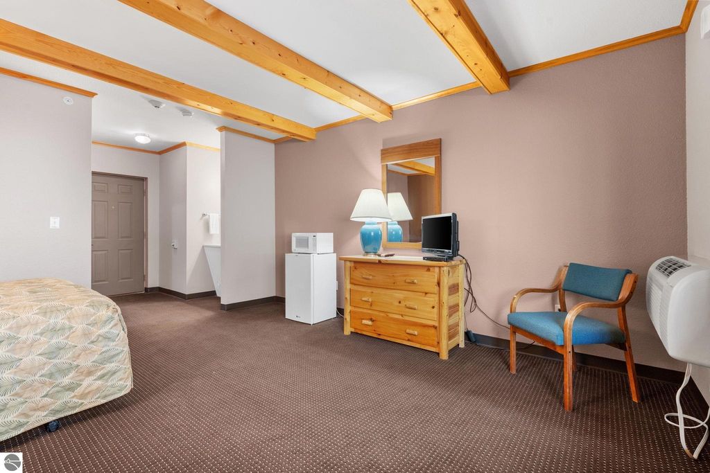 Updated motel room featuring wooden beams, a bed with patterned bedding, dresser with television, lamp, chair, and microwave, highlighting investment potential near Torch Lake.