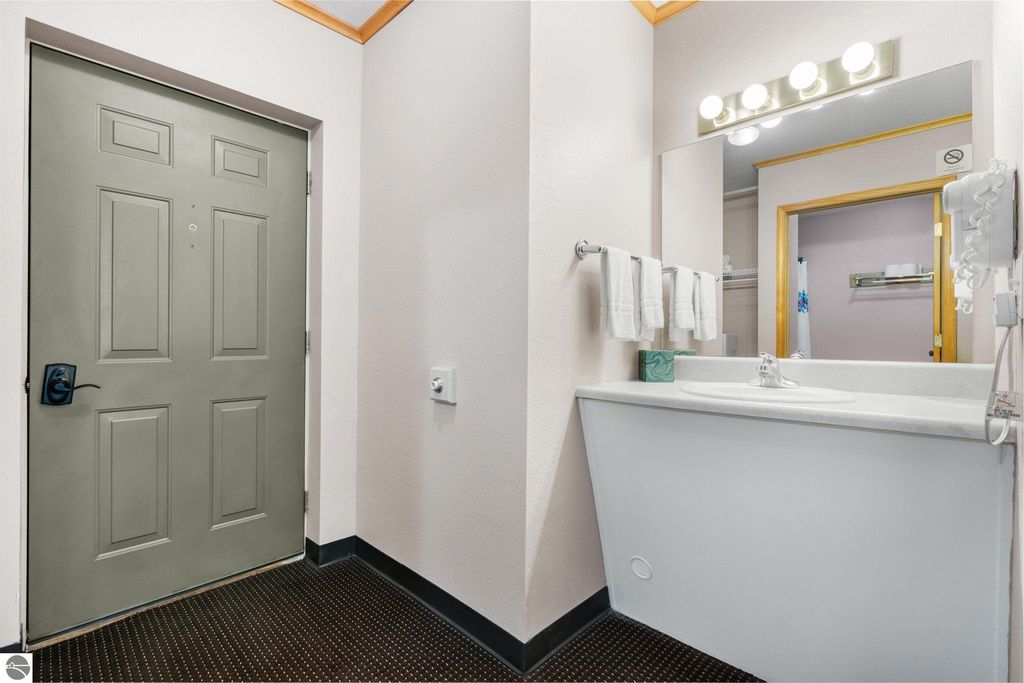 Entrance view of a motel room featuring a green door, sink area with towels, and a well-lit mirror, highlighting the updated accommodations near Torch Lake.