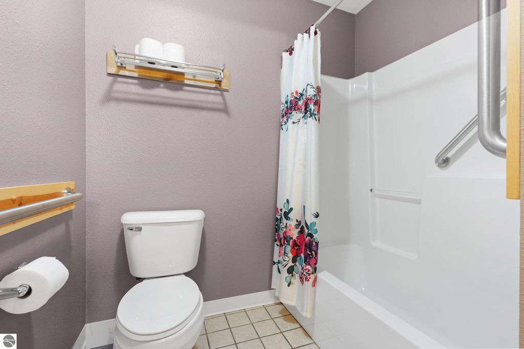 Updated bathroom with purple walls, floral shower curtain, toilet, and grab bars, designed for motel accommodations near Torch Lake.