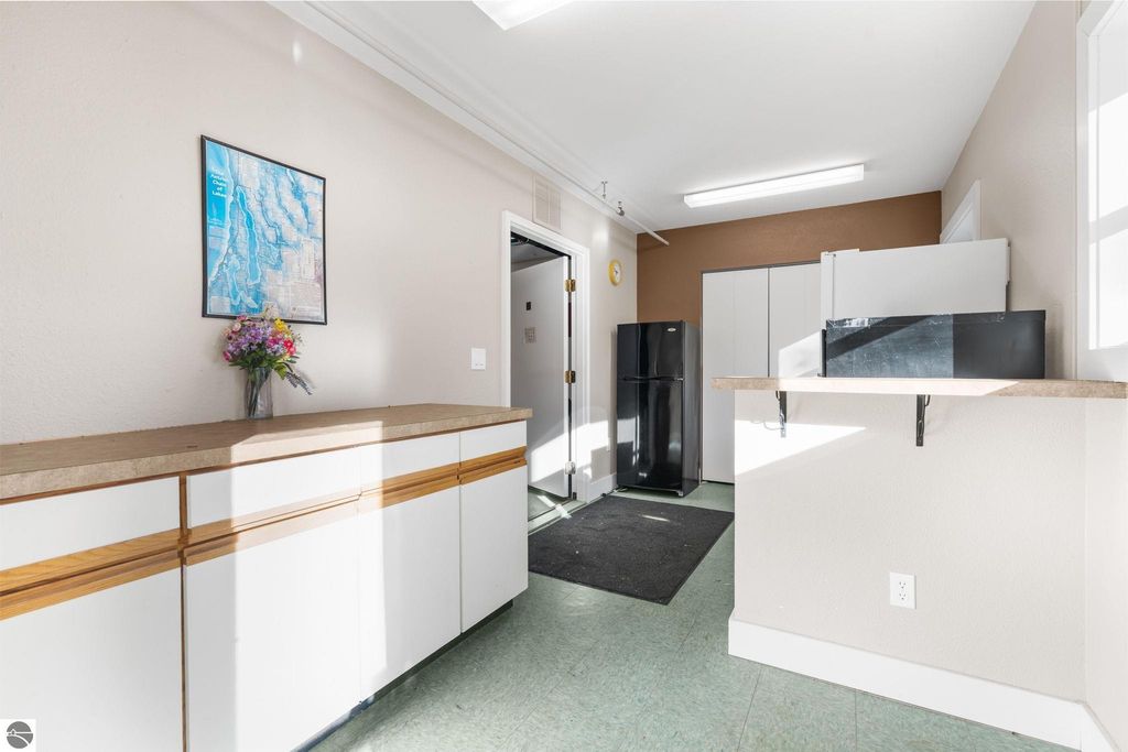 Interior view of a motel lobby featuring a reception desk with a countertop, a black refrigerator, and a wall-mounted map, emphasizing the property’s welcoming atmosphere for guests at the resort near Torch Lake.