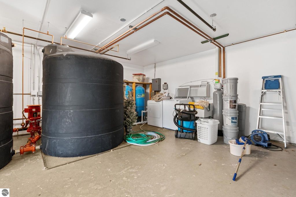 Utility room with large black water tanks, laundry appliances, cleaning supplies, and plumbing fixtures, highlighting essential infrastructure for the motel and home at 12800 & 12862 Cherry Avenue, Rapid City, MI.