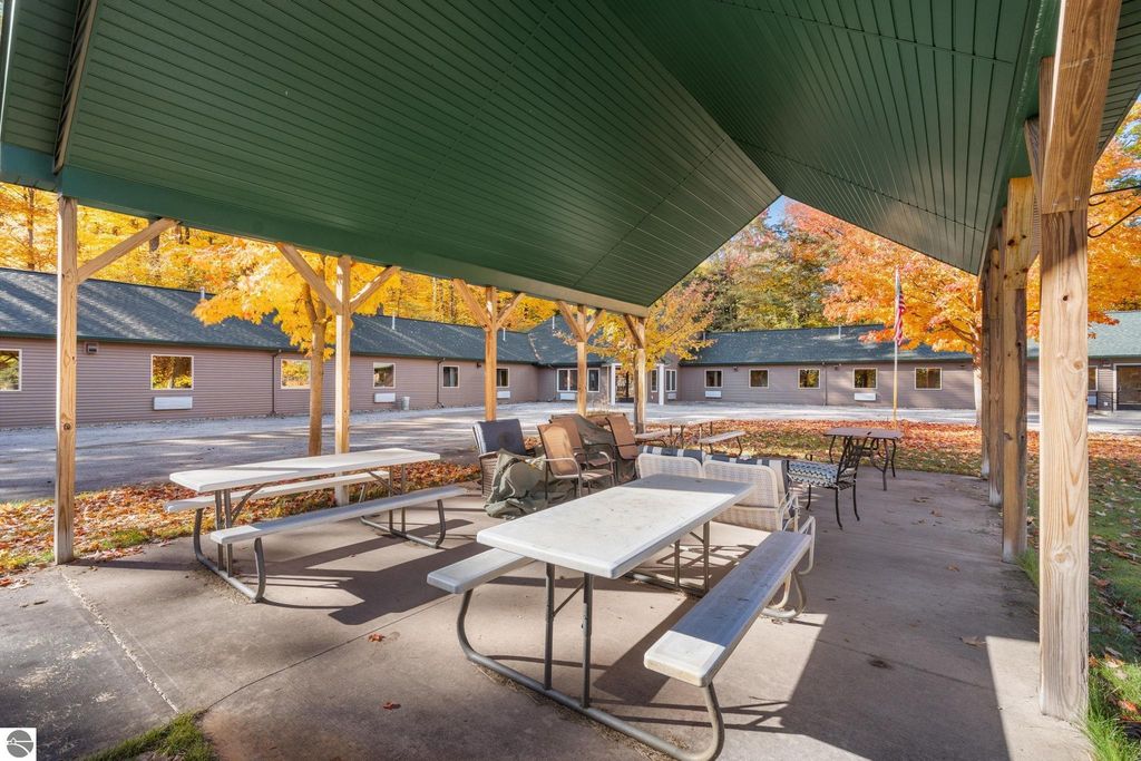 Covered outdoor seating area with picnic tables and chairs, surrounded by autumn foliage and motel units, showcasing a resort property near Torch Lake, Rapid City, MI.
