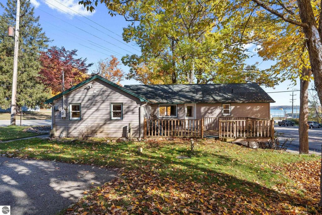 Exterior view of a 3-bedroom, 2-bath home with a wooden deck, surrounded by colorful autumn foliage, located near Torch Lake, Michigan, suitable for manager accommodations or rental income.