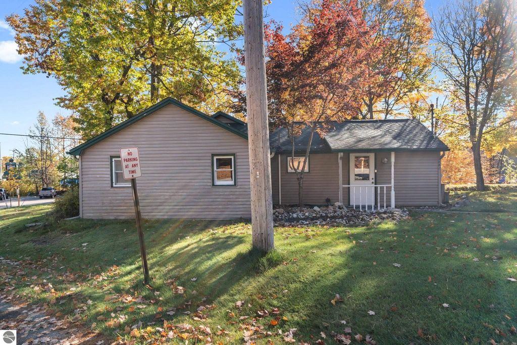 Single-story home with a pitched roof, surrounded by autumn foliage, featuring a 'No Parking at Any Time' sign, located near Torch Lake in Rapid City, MI, ideal for on-site management or rental opportunities.