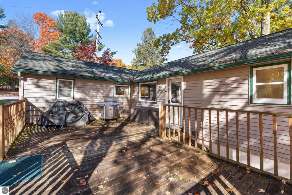 Exterior view of a home at 12800 & 12862 Cherry Avenue, featuring a wooden deck, grill, and autumn foliage, highlighting the property’s appeal for potential buyers and rental opportunities near Torch Lake.