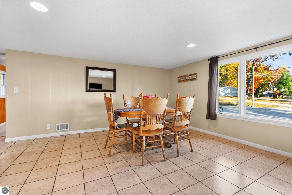 Dining area with a large wooden table and chairs, bright natural light from windows, showcasing a cozy interior suitable for a resort property near Torch Lake in Rapid City, MI.