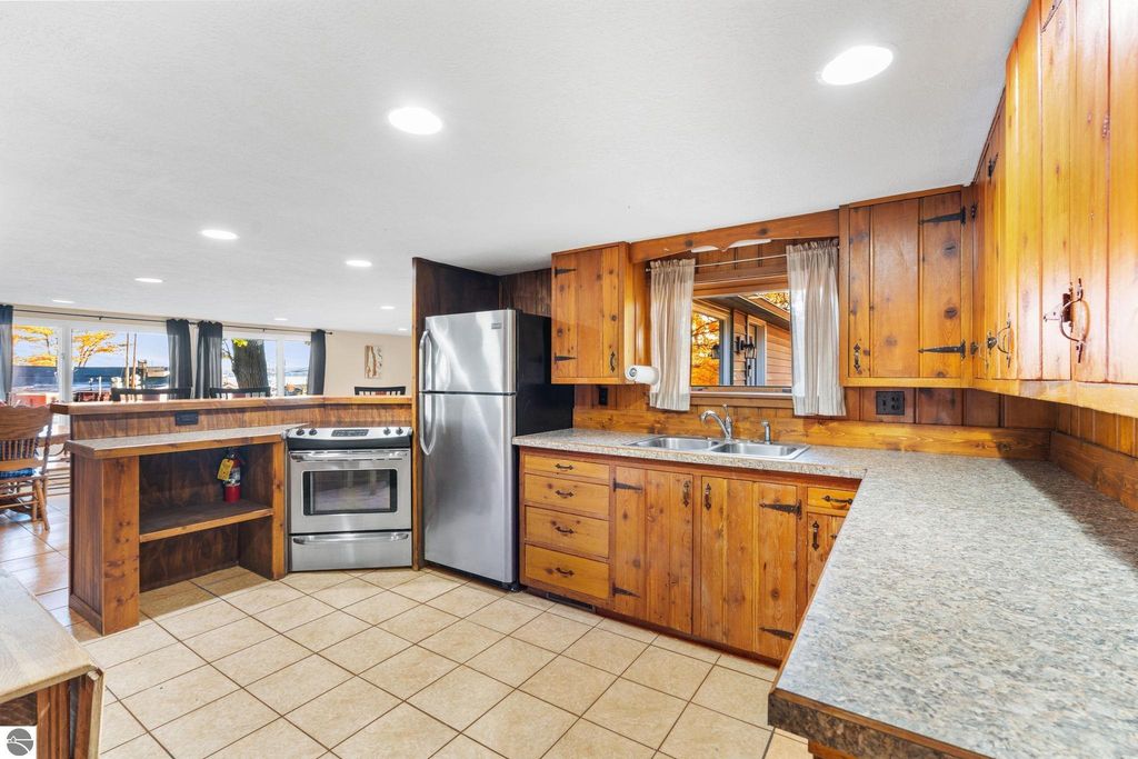 Updated kitchen with wooden cabinetry, stainless steel appliances, and tile flooring, featuring a view of Torch Lake through large windows, ideal for a resort property at 12800 & 12862 Cherry Avenue, Rapid City, MI.