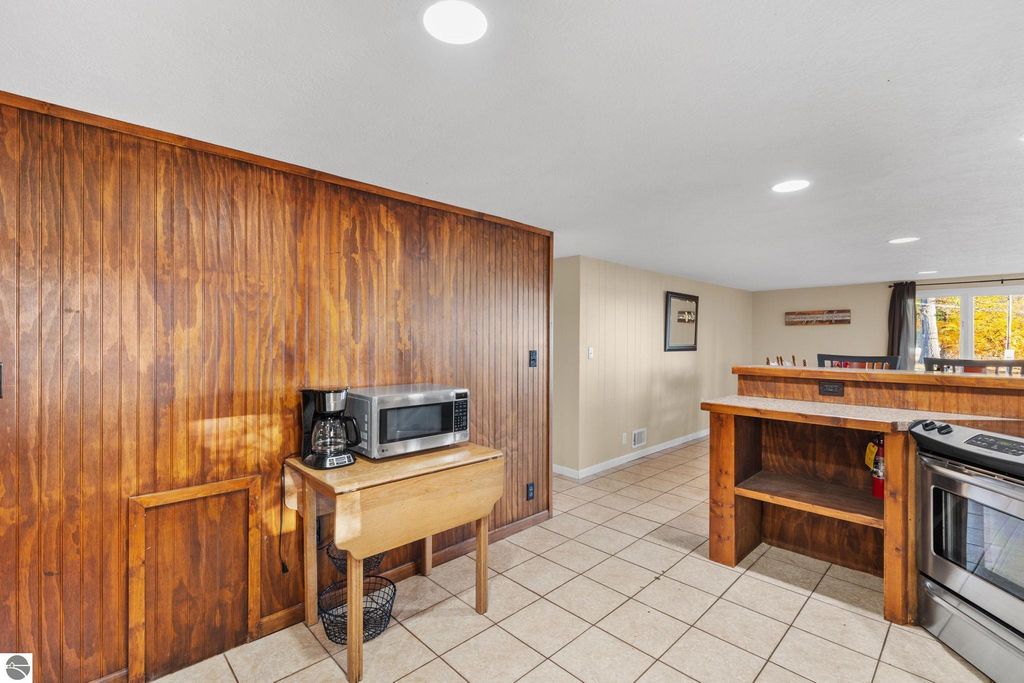 Interior view of a kitchen area featuring wooden cabinetry, a microwave, coffee maker, and tile flooring, showcasing the updated amenities of a resort property near Torch Lake.