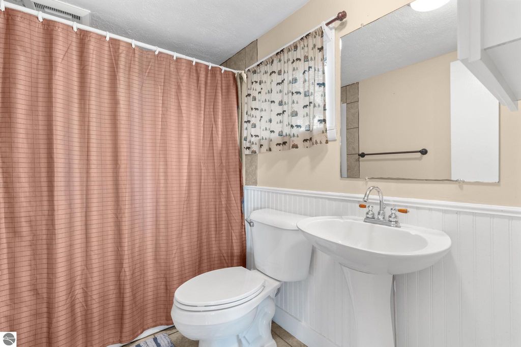 Bathroom interior featuring a pink striped shower curtain, white toilet, and sink with a mirror, showcasing a clean and updated space ideal for guests at the motel property near Torch Lake.