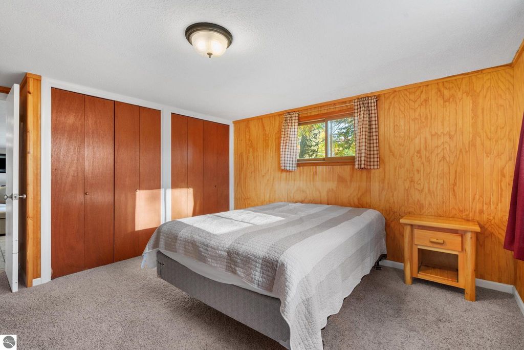 Cozy bedroom featuring a queen-sized bed, wooden paneling, and natural light from a window, part of a property listing at 12800 & 12862 Cherry Avenue, Rapid City, MI.