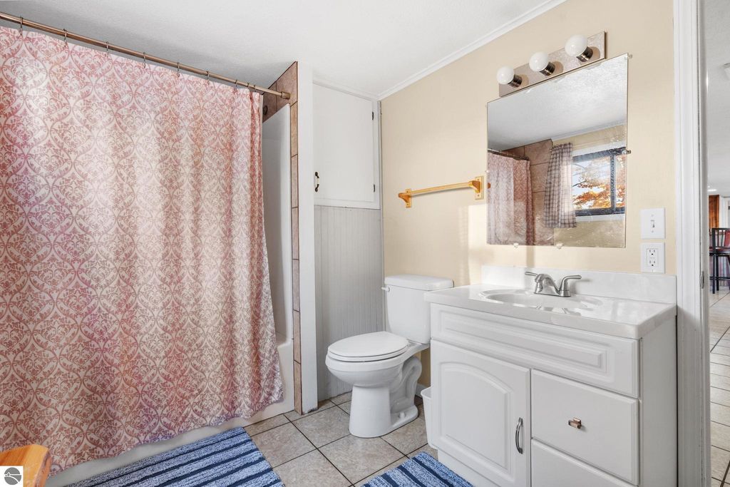 Bathroom interior featuring a white vanity with sink, a toilet, patterned shower curtain, and a window, highlighting updated accommodations in a resort property near Torch Lake, Rapid City, MI.