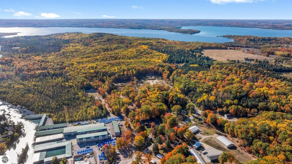 Aerial view of vibrant autumn foliage surrounding Torch Lake, showcasing wooded areas, water bodies, and nearby structures, highlighting the scenic location of the resort property at 12800 & 12862 Cherry Avenue, Rapid City, MI.