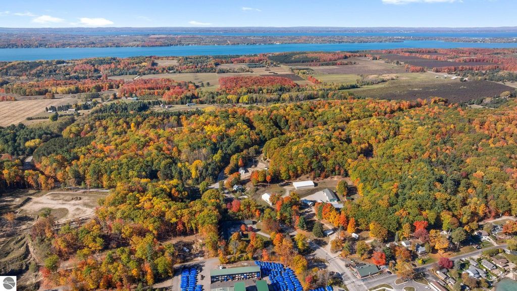 Aerial view of vibrant autumn foliage surrounding Torch Lake, showcasing nearby properties and open land in Rapid City, MI, emphasizing the scenic landscape and investment potential near the resort property.