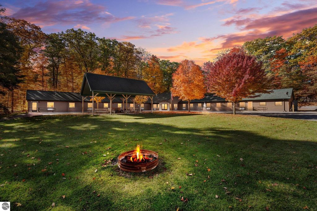 Resort property exterior featuring a modern motel building surrounded by colorful autumn trees, fire pit in foreground, showcasing a tranquil setting near Torch Lake, Rapid City, MI.