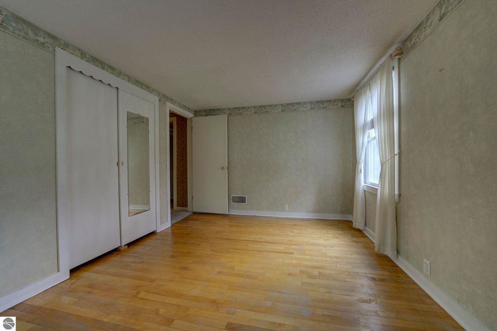 Spacious interior view of a well-maintained bedroom with hardwood flooring, large windows, and built-in mirrored closet doors, showcasing the inviting atmosphere of the home at 624 Fenton Street, Kingsley, MI.